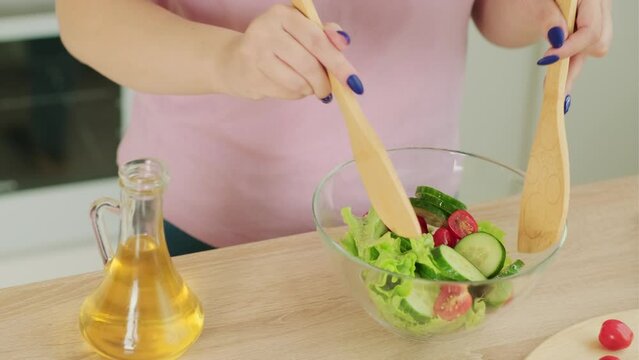 Unrecognizable woman preparing vegetable salad in kitchen. Body part of female stirring salad with kitchen wooden spatulas.