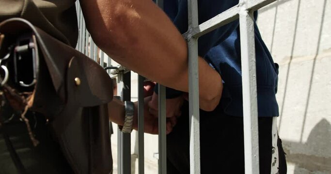 a policeman puts handcuffs on a prisoner behind bars in a prison cell. a soldier with a pistol and a holster on his belt removes the terrorist's handcuffs. close-up