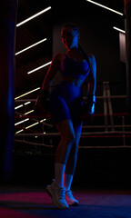 Powerful girl poses near the bag on the background of the ring. Color flashes. The concept of wrestling and boxing.