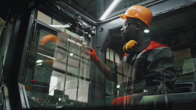 Professional Black male technician engineer connecting wires in tractor machine while working at industrial plant