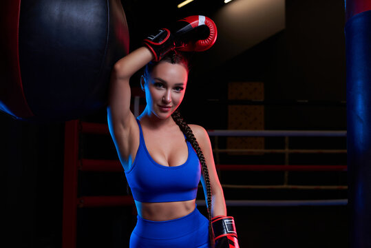 Image of a powerful sportswoman wrestler. Posing in a blue tracksuit and red boxing gloves. The concept of wrestling and boxing.