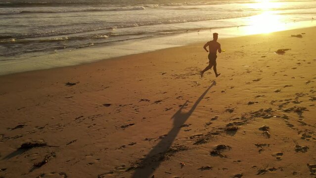 Aerial shot of a Athletic African American Man jogging on the beach at sunset