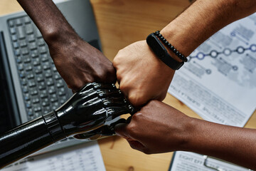 Above shot of hands of young intercultural coworkers including employee with myoelectric arm making...