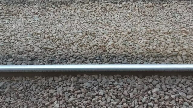 Tram rails on brownish gray stones. On dry granite stones scattered with small chips, metal rails for the tram are laid parallel to each other. The camera moves to the right along.