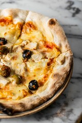 Vertical shot of a thick-crust pizza with chicken breast, cheese, seasoned olives on marble surface