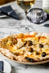 Vertical shot of thick-crust pizza with chicken breast, cheese, seasoned olives on marble surface