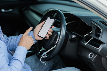 Naklejka premium Close-up shot of the driver using a smartphone with a blank white screen inside the car. Man looking at location, finds smartphone screen through gps navigator application.