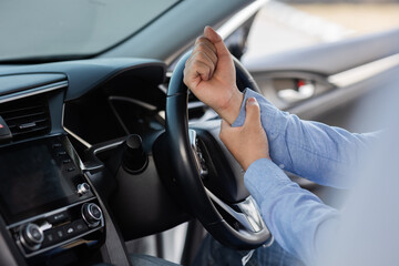 Concept : wrist pain from long driving. Middle-aged man holds his wrist and sits in car. Feeling painful.