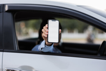 Mock up view of man holding and showing mobile phone with blank screen while sitting in car