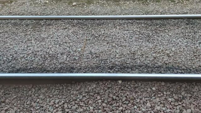 Tram rails on brownish gray stones. On dry granite stones scattered with small chips, metal rails for the tram are laid parallel to each other. The camera moves to the right along.