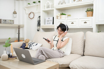 Obraz premium An Asian teenager wearing headphones enjoying music at home