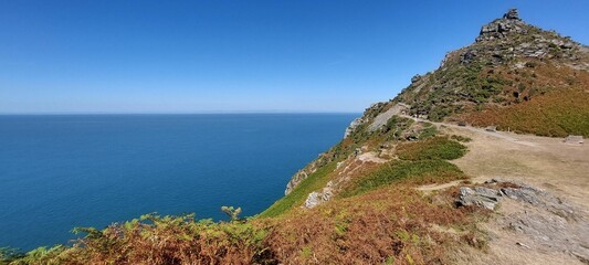 Lush green vegetation on steep rocky cliff overlooking the clear blue sea in England