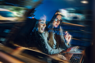 Two multiracial business woman riding in a car and using a laptop
