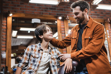 Smiling hairdresser looking at teenage boy in barbershop.