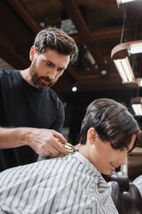 bearded barber trimming neck of teenage boy with hair clipper.