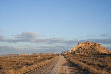 Gravel road that disappears into the horizon towards the Bardenas Natural Park. Semi-desert landscape in the north of Spain, Navarra.