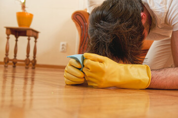 Depressed man, stressed out from housework, falling down exhausted from cleaning, holding a piece of cloth in his hands