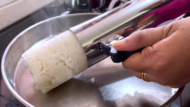 Closeup on a woman's hands preparing a Steam cooked Indian breakfast Puttu and serving on plate