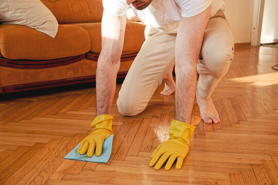 Handsome man cleaning floor in his house with a piece of cloth and using gloves, working hard