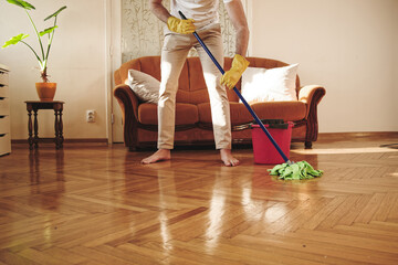 Young man mopping or swiping the floor with his mop handle, broom, cleaning his living room