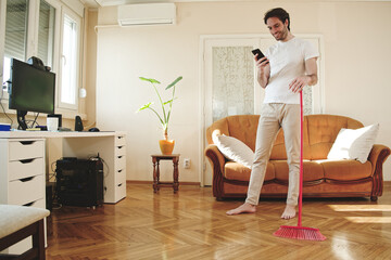 Handsome man holding standing, holding his broom and having chat on his phone at the home - 545245166