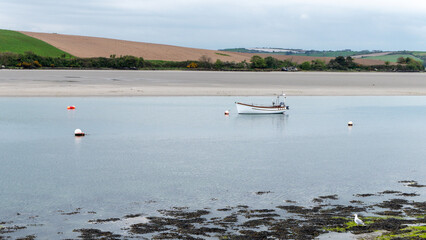 A small motor boat moored in shallow water. Calm water surface. Picturesque hills on the shore of the bay. The sandy shore of the Atlantic Ocean.