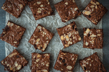 Delicious homemade chocolate brownies with almond flakes and raisins cut on square slices on the baking parchment. Flat lay. Grey concrete background