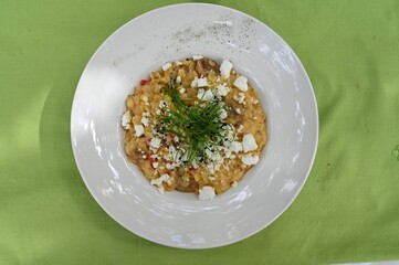 White round plate with feta risotto and herbs on top on a green background
