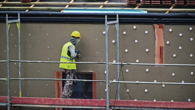 Construction Worker Standing on Scaffolding Drilling Hole in Wall Plasterwork