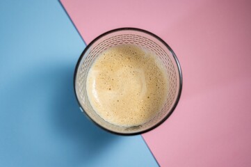 Top view of a glass of coffee on a blue and pink background