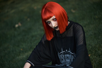 Young urban goth girl with a red hair wig posing outdoors, representing alternative subculture - 545251132