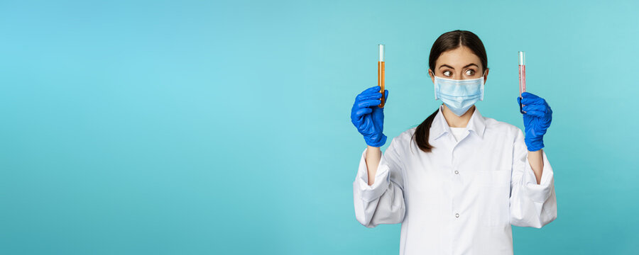 Image Of Young Woman Doctor, Lab Worker Doing Research, Holding Test Tubes, Wearing Medical Face Mask And Rubber Gloves, Blue Background