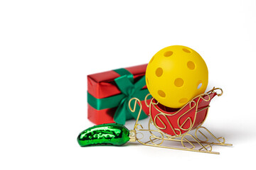 Yellow Christmas Pickleball in a red Santa sleigh with Christmas Pickle ornament and wrapped gift...