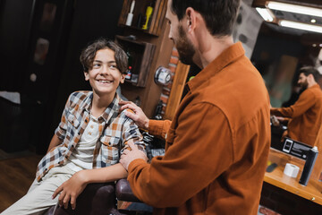 Fototapeta na wymiar Cheerful teenager looking at blurred barber in barbershop.