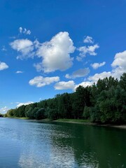 Vertical shot of a river with a green trees and blue cloudy sky