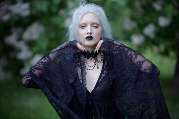 Dark goth girl standing in the forest, portrait of a wiccan witch performing magic