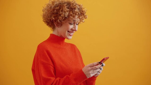 Lovely curly haired adult ginger woman texting on phone in the yellow studio