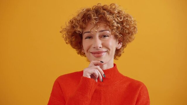 Pensive curly haired adult ginger woman thinking about something in the yellow studio