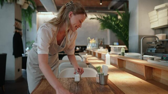 Smiling blonde woman waitress wiping the tables in the cafe