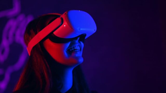 A young woman in VR glasses is smiling while playing VR games. Red and blue illumination. Slow motion