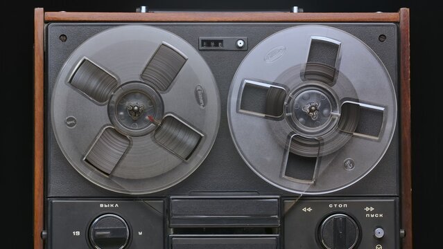 Vintage reel to reel tape recorder on black studio background. Retro music player with old plastic bobbins. Analog antique record player with magnetic tape reel for playing music. Front view close up.