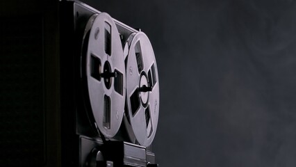 Reel to reel tape recorder on black studio background with smoke. Analog antique record player with...