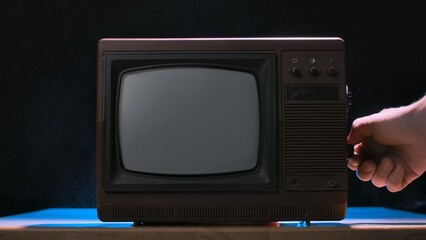 Man turning knob on an old retro TV on black studio background. Vintage analog television. Brown...