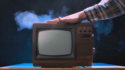 Male hand wiping dust from the surface of an old vintage TV. Retro TV set with the screen turned...