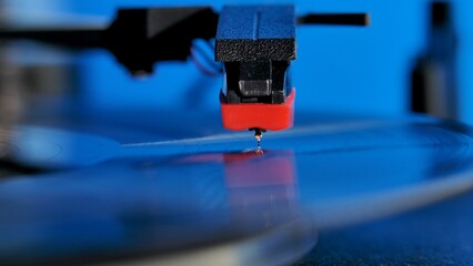 Vinyl record disc spinning on the classic gramophone player against colorful background. Vinil turntable plays the popular music from plate. Macro shot of needle head playing record in blue neon light