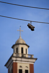 Fototapeta na wymiar Pair of Sneakers Hanging on the Cable With Bell Tower on Background