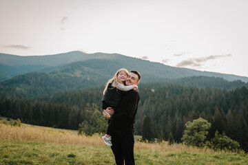 Child hugging father and playing in the park at the sunset time. Concept of friendly family. Father's Day. Portrait dad and daughter in mountains on summer or autumn vacation. Place for text. Closeup.