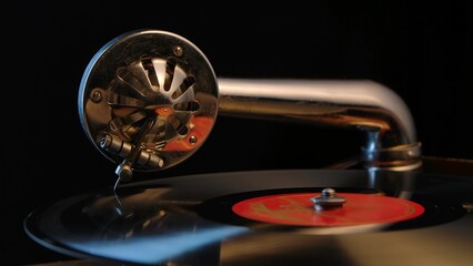 Vintage old record player gramophone needle on vinyl record. Round shiny metal needle holder head reproducing music. Retro vintage vinyl player on black background. Needle old gramophone close up.