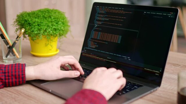 Close up of freelancer's hands typing code on laptop keyboard. Camera slides around developer's figers writing program code on computer display. Programmer working on online application database.