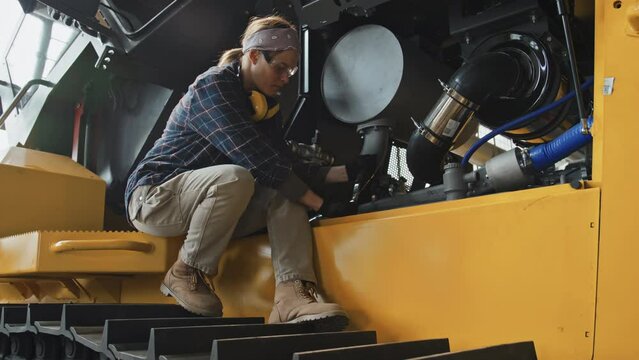 Female mechanic sitting on tractor while repairing machine at vehicle production plant